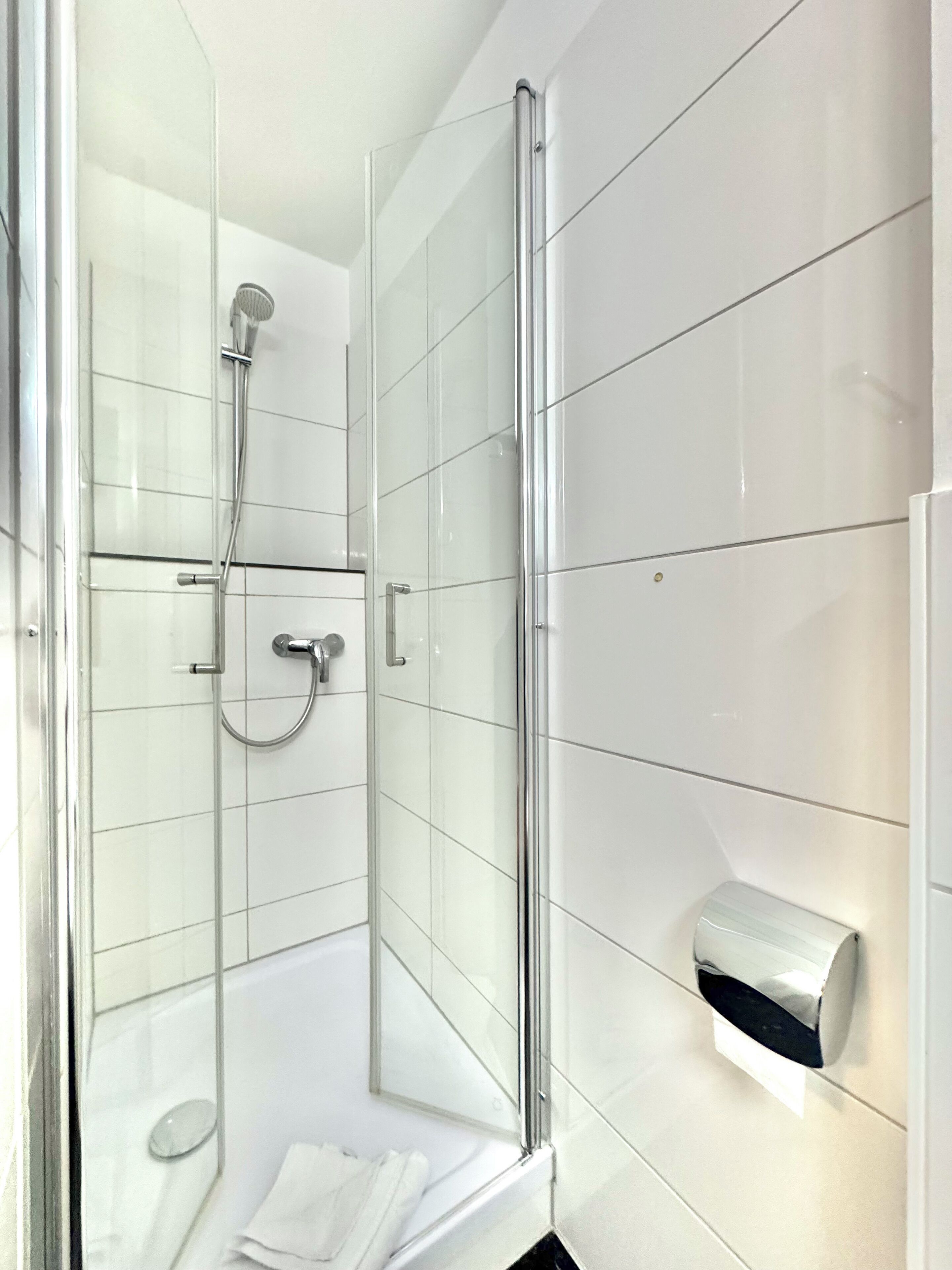 Een moderne badkamer met een douchecabine van glas, een handdouche en een muurbevestigde handdoekdispenser.