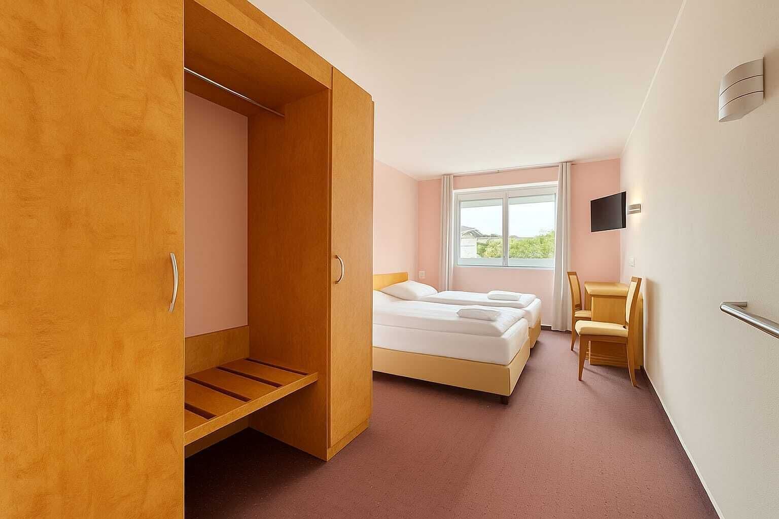 A hotel room with a wooden wardrobe, a bed, a desk, and a chair.