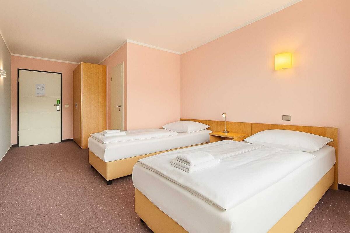Une chambre d’hôtel avec deux lits, une armoire en bois, une porte avec une serrure et un luminaire fixé au mur.