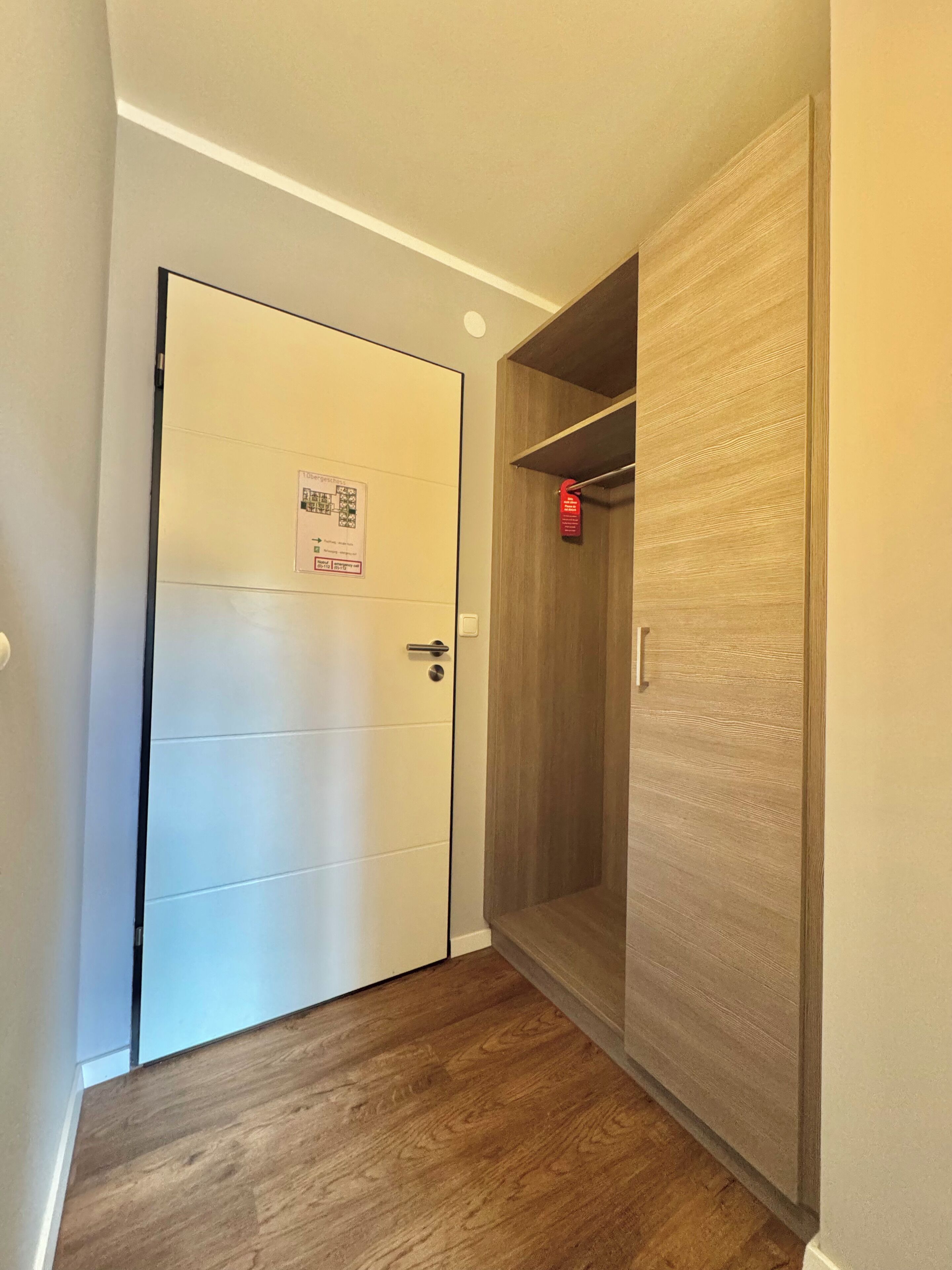 Ein Flur mit einer weißen Tür, einem Holzschrank und einem roten Rauchmelder.