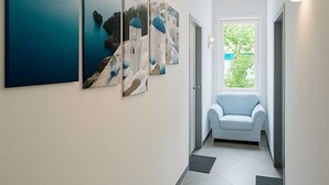 Um corredor com piso de azulejos, um sofá azul-claro e três quadros na parede.