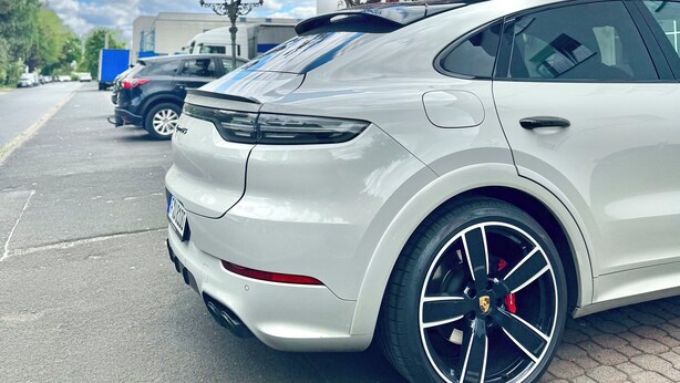 Um carro branco estacionado num parque de estacionamento, com um edifício ao fundo.