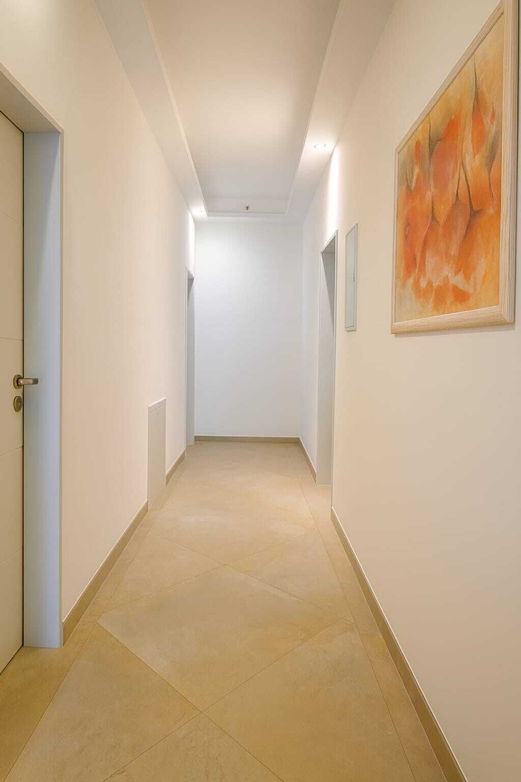 A hallway with a tiled floor, white walls, and a door on the left.