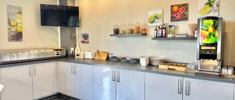 Una cocina moderna con una televisión de pantalla plana, una cafetera y diferentes electrodomésticos.