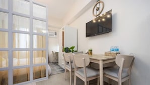 Una habitación moderna con comedor, televisor montado en la pared y un amplio ventanal con cortinas.