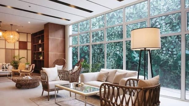 Una sala moderna con un ventanal grande, muebles de mimbre y una lámpara de pie.