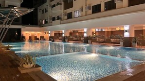 Una piscina con suelo de baldosas, rodeada de sillones de descanso y plantas en macetas.