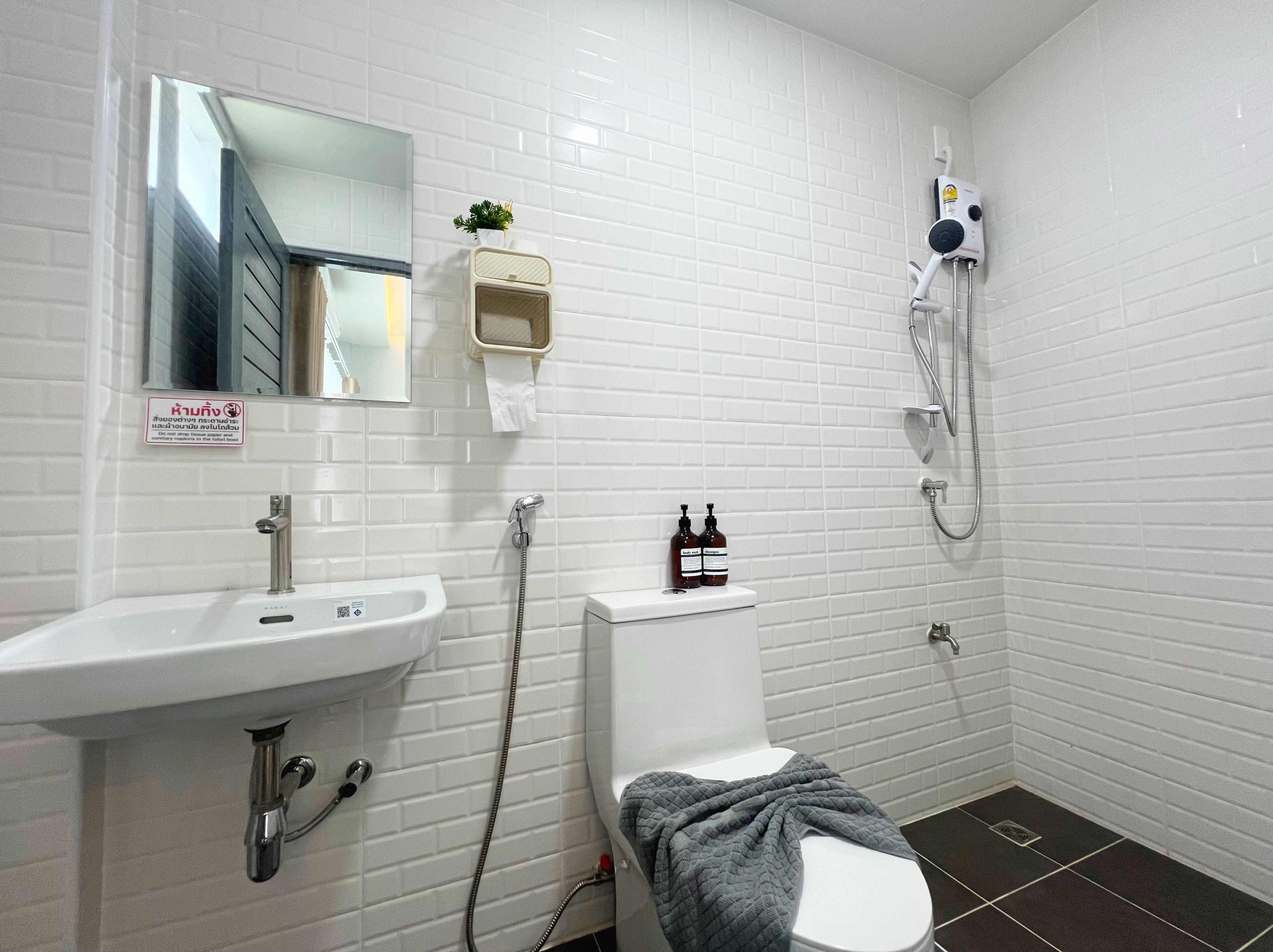 A bathroom with a white sink, toilet, and shower. There is a mirror above the sink and a sign on the wall.