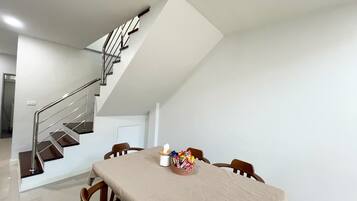 A modern interior with a dining table set for four, a staircase, and a white wall.
