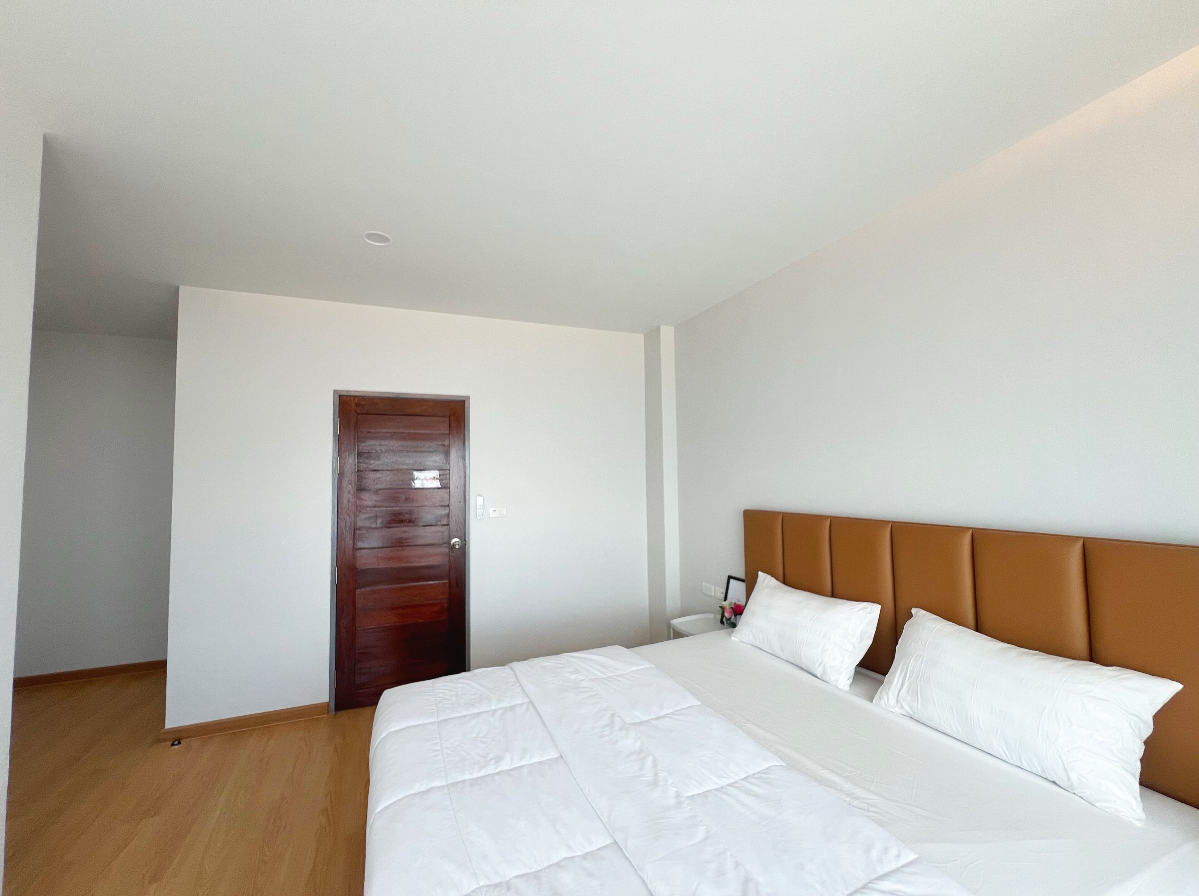 Habitación de hotel con una cama grande, una puerta de madera y una pared blanca.