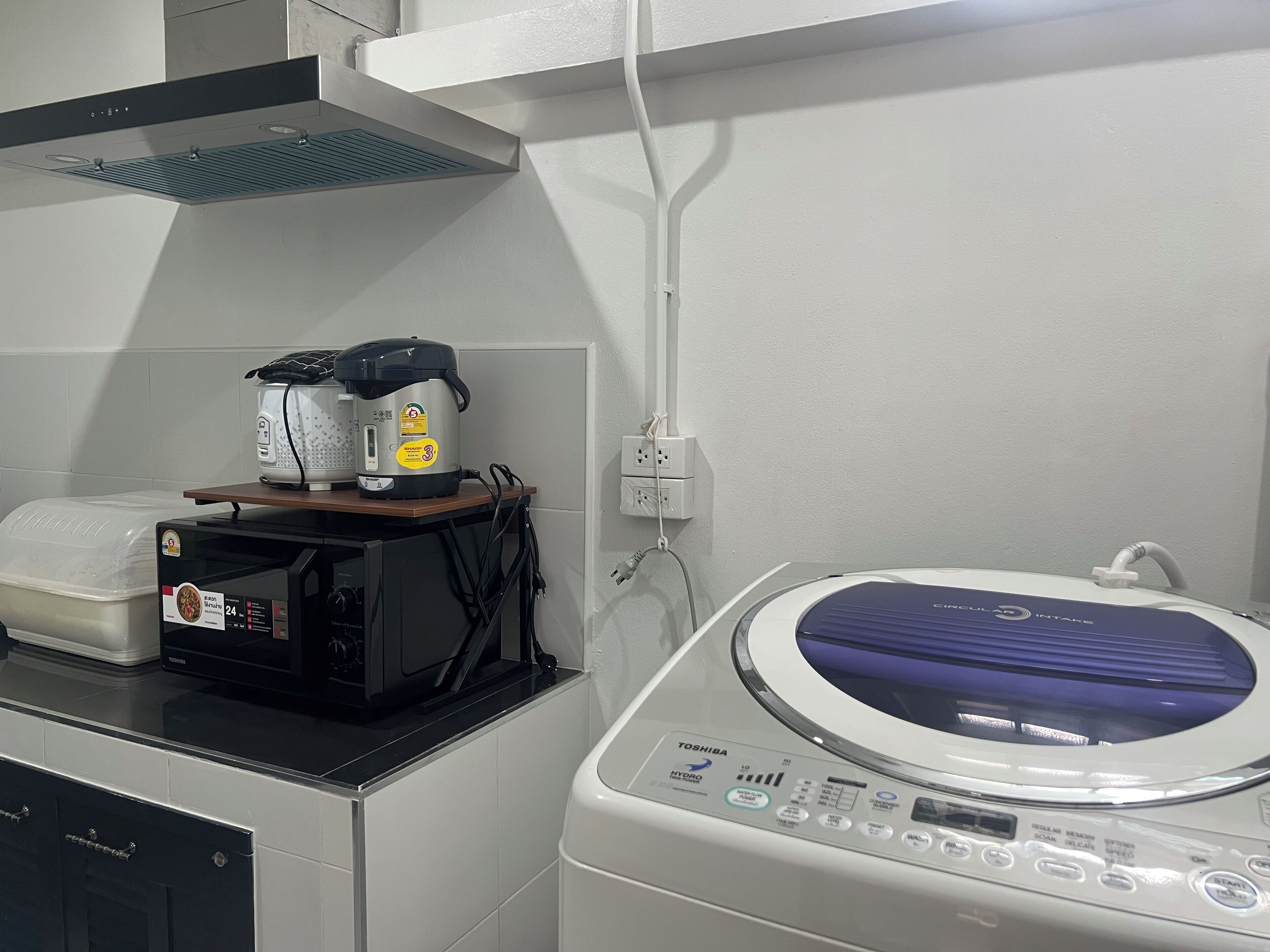 A kitchen with a washing machine, a rice cooker, and a microwave.