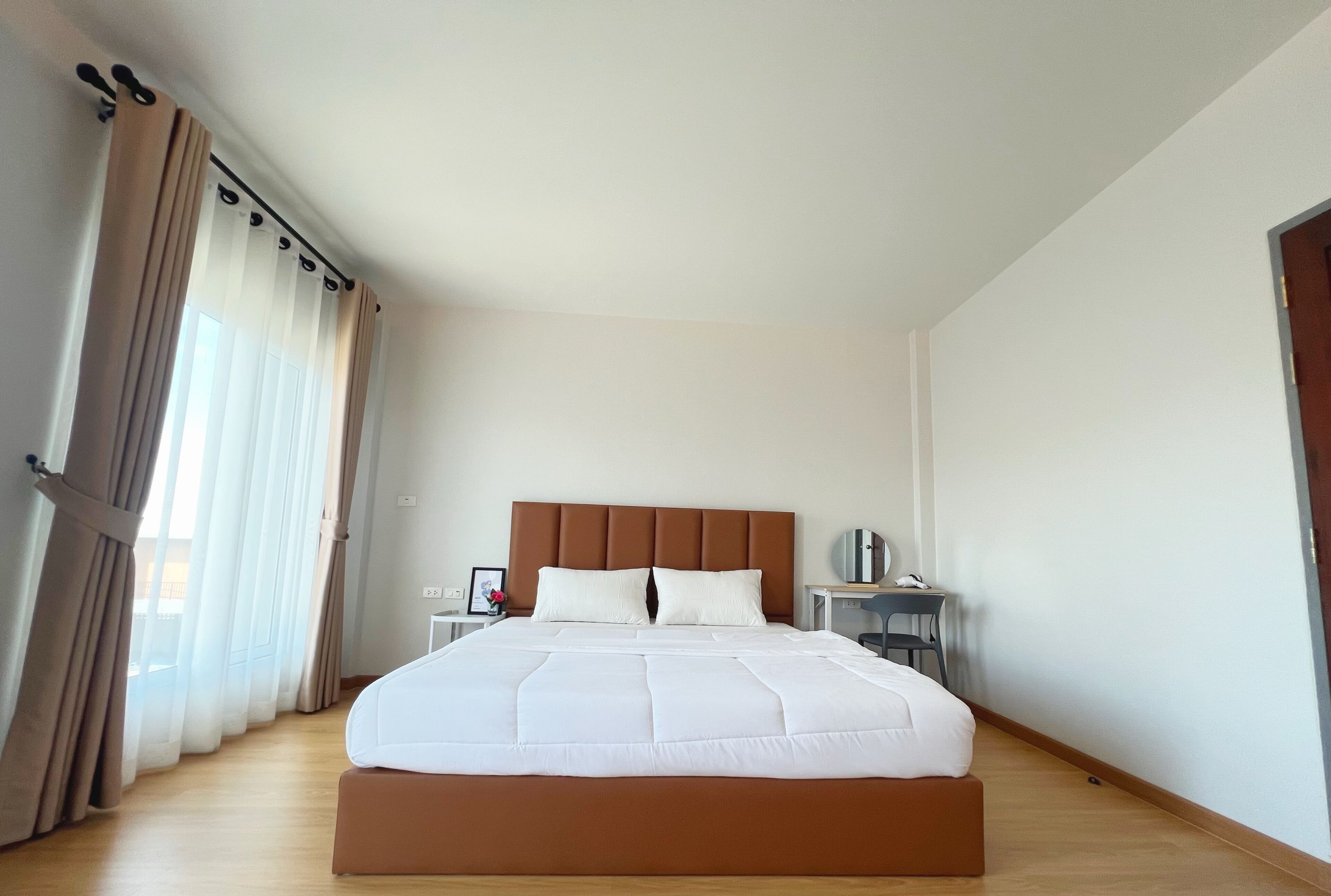 A modern hotel room with a large bed, a wooden floor, a nightstand, and a desk with a chair.