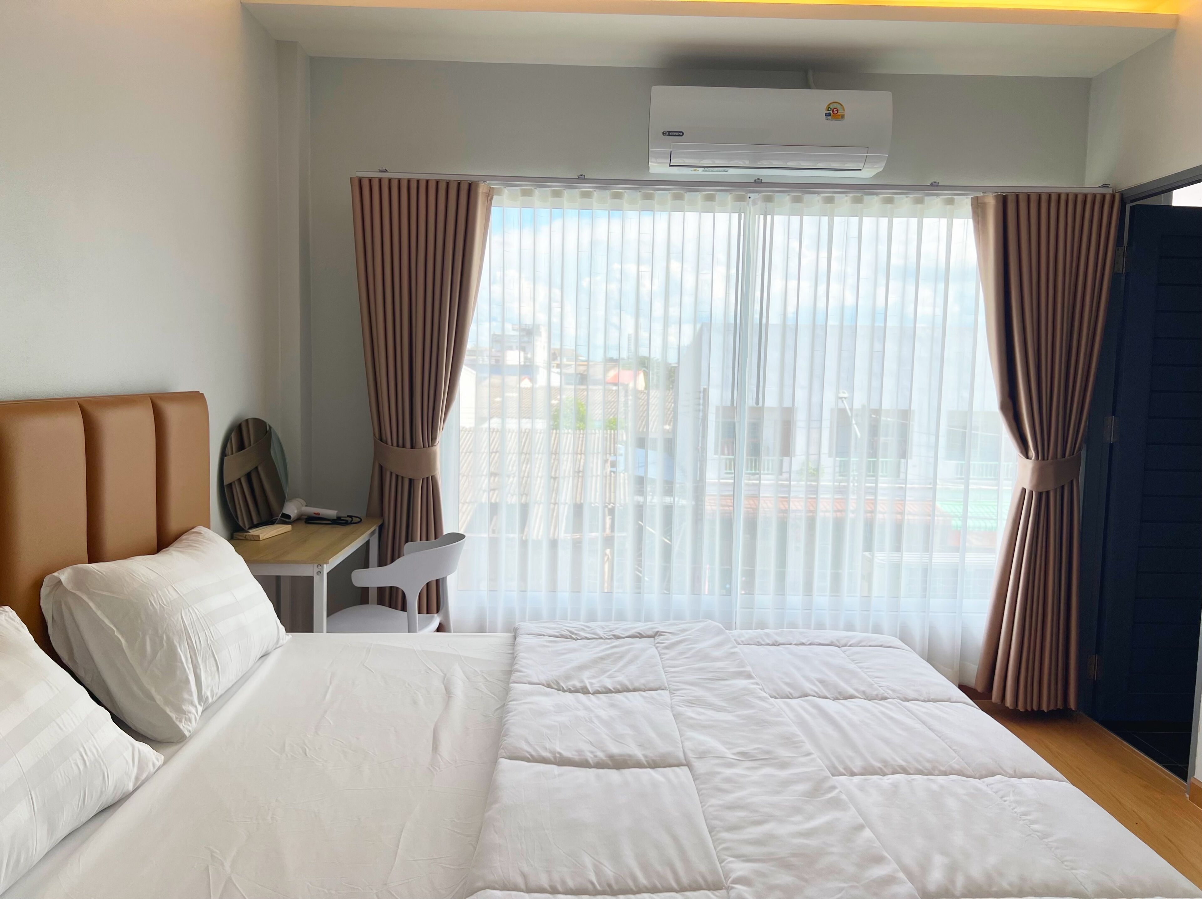 Een hotelkamer met een groot bed, een bureau en uitzicht op de stad door dunne gordijnen.