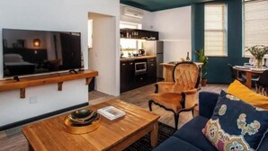 A compact living space with a TV mounted on the wall, a wooden coffee table, a sofa with colorful cushions, a kitchen area with a dining table, and a chair. - 4 Executive self catering Apartments, two with private hot tubs. (Cape Town)