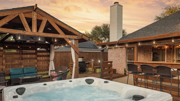 A hot tub with a wooden deck, a barbecue area, and outdoor seating. - 2 minutes from lake, Pickleball, Hot Tub, Pool table! (Rowlett)