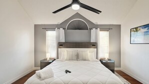 A bedroom with a large bed, a ceiling fan, two bedside tables, and a nightstand. - 2 minutes from lake, Pickleball, Hot Tub, Pool table! (Rowlett)