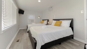 A hotel room with two beds, a flat-screen TV mounted on the wall, and a ceiling light.