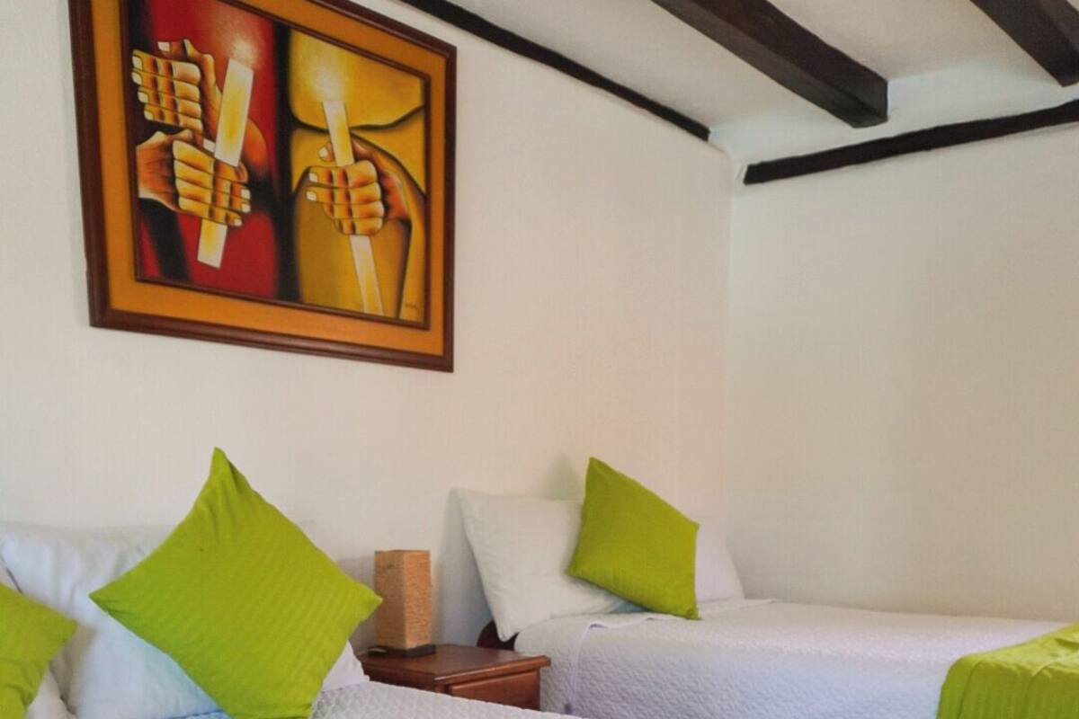Une chambre d’hôtel avec deux lits, chacun recouvert d’une couette verte et doté de draps blancs. Un tableau est accroché au mur, au-dessus des lits.