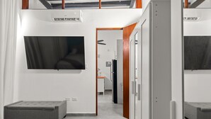 Une chambre d’hôtel moderne dotée d’un téléviseur à écran plat fixé au mur, d’un petit coin salon et d’une porte donnant sur un couloir.