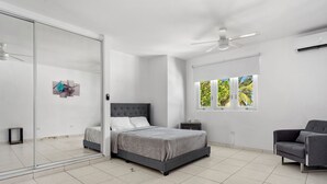 Una camera da letto moderna con un letto, una sedia, un comodino, una finestra vista alberi e una ventola a soffitto.