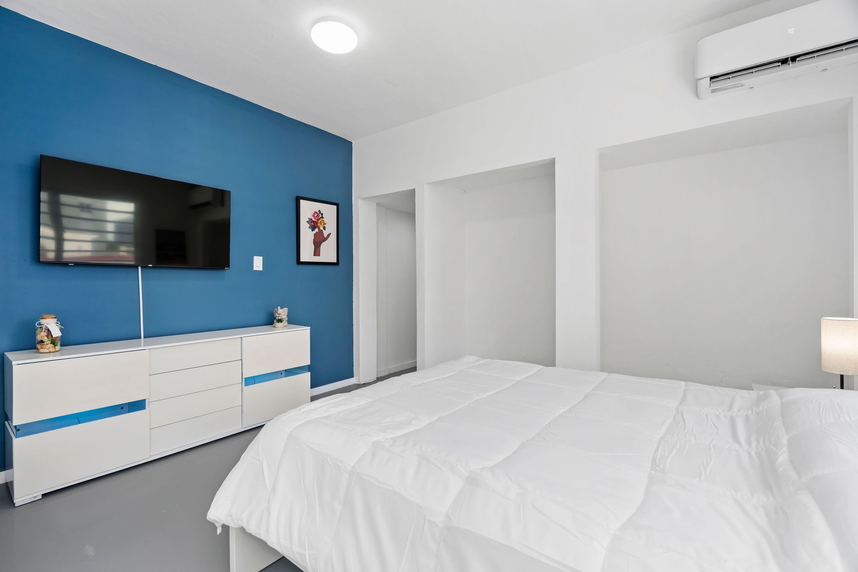 Un dormitorio con una cama grande, un televisor montado en la pared, un aparador y un cuadro enmarcado.