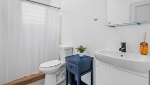 Une salle de bain comprenant des toilettes, un lavabo, un miroir et une petite table sur laquelle est posée une plante.