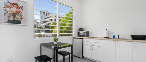 A modern kitchen with white cabinets, a black countertop, a microwave, and a small dining table with two chairs.