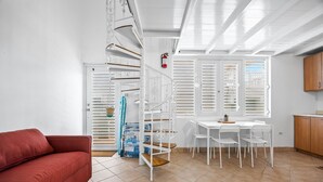 A modern kitchen with white cabinetry, a dining table with chairs, a red sofa, and a spiral staircase. - Beachfront With Pool Free Parking (Aguada)