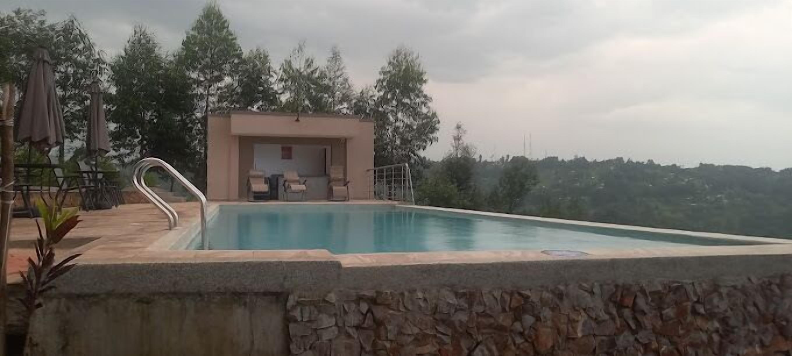 A swimming pool with a stone wall, a covered seating area, and trees in the background.