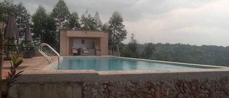 A swimming pool with a stone wall, a covered seating area, and trees in the background.
