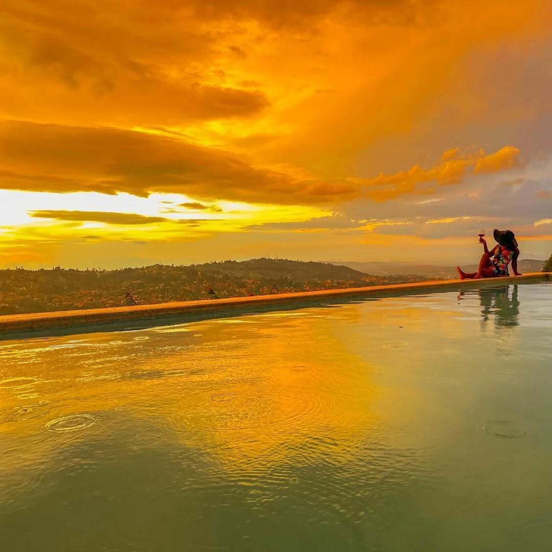 Una persona sentada junto a una piscina con vistas al atardecer.
