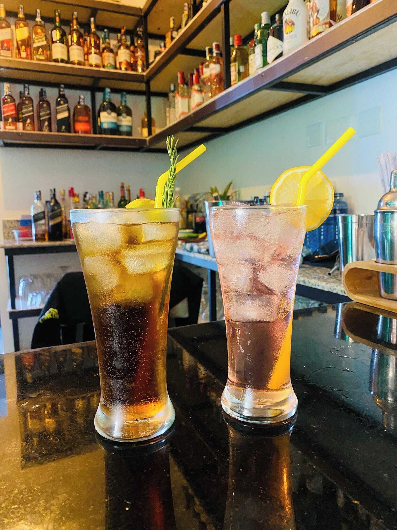 Zwei Gläser gekühlte Getränke mit Zitronenscheiben und Rosmarinzweig auf einer Bar.