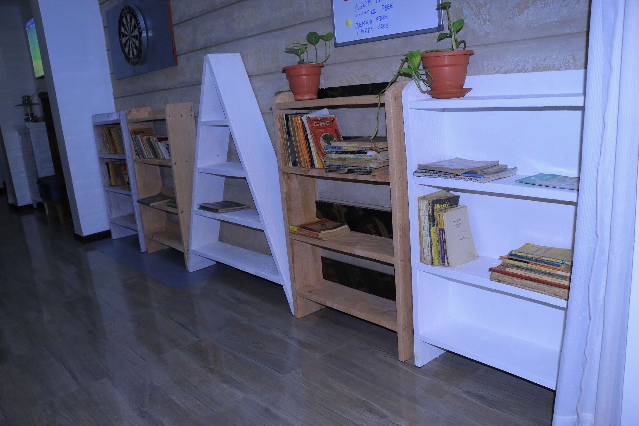 Un pasillo con estanterías de madera, algunas con libros y plantas en macetas, y un dardo en la pared.