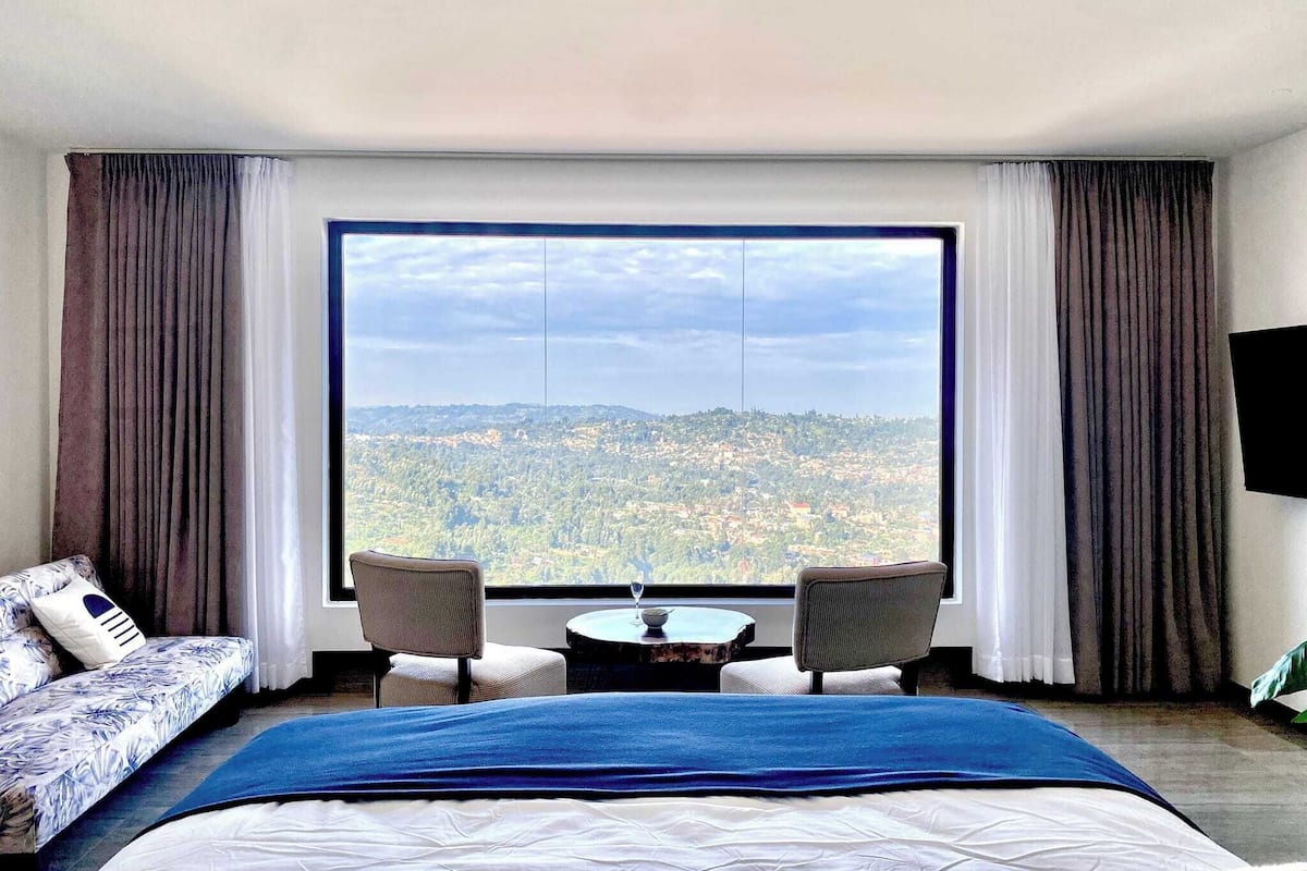 A hotel room with a large window, a bed, two chairs, and a small table.