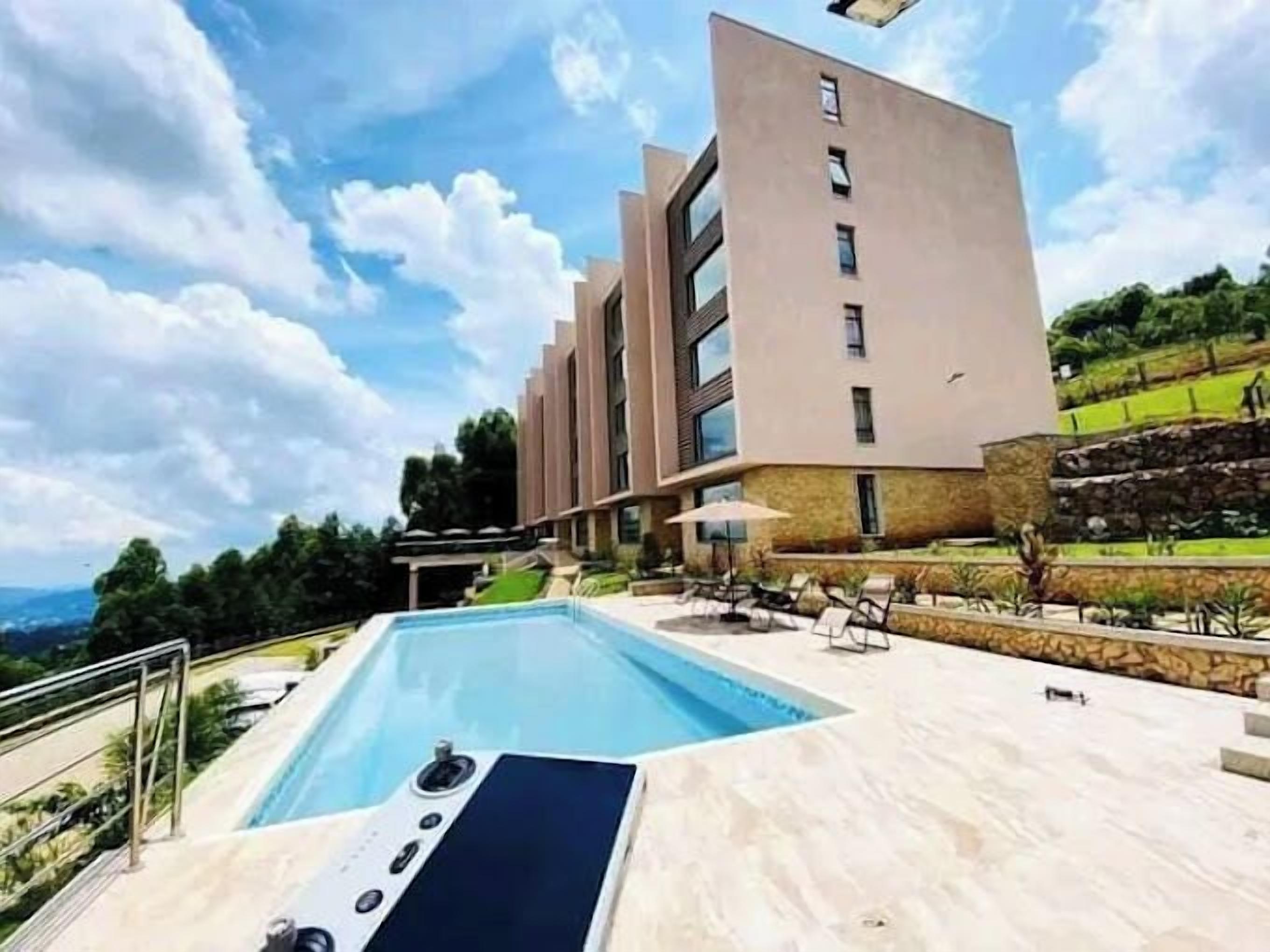 A modern building with a pool area, including a pool with a control panel, lounge chairs, and a stone wall.