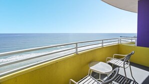 A balcony with a yellow wall, a purple wall, and a white railing overlooking the ocean.