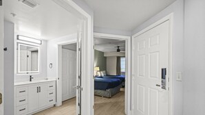 Una habitación de hotel con baño, una cama con ropa de cama azul y un ventilador de techo.