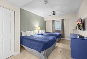 Et hotelværelse med to senge, et skrivebord, en loftsvifte og et vindue med gardiner.