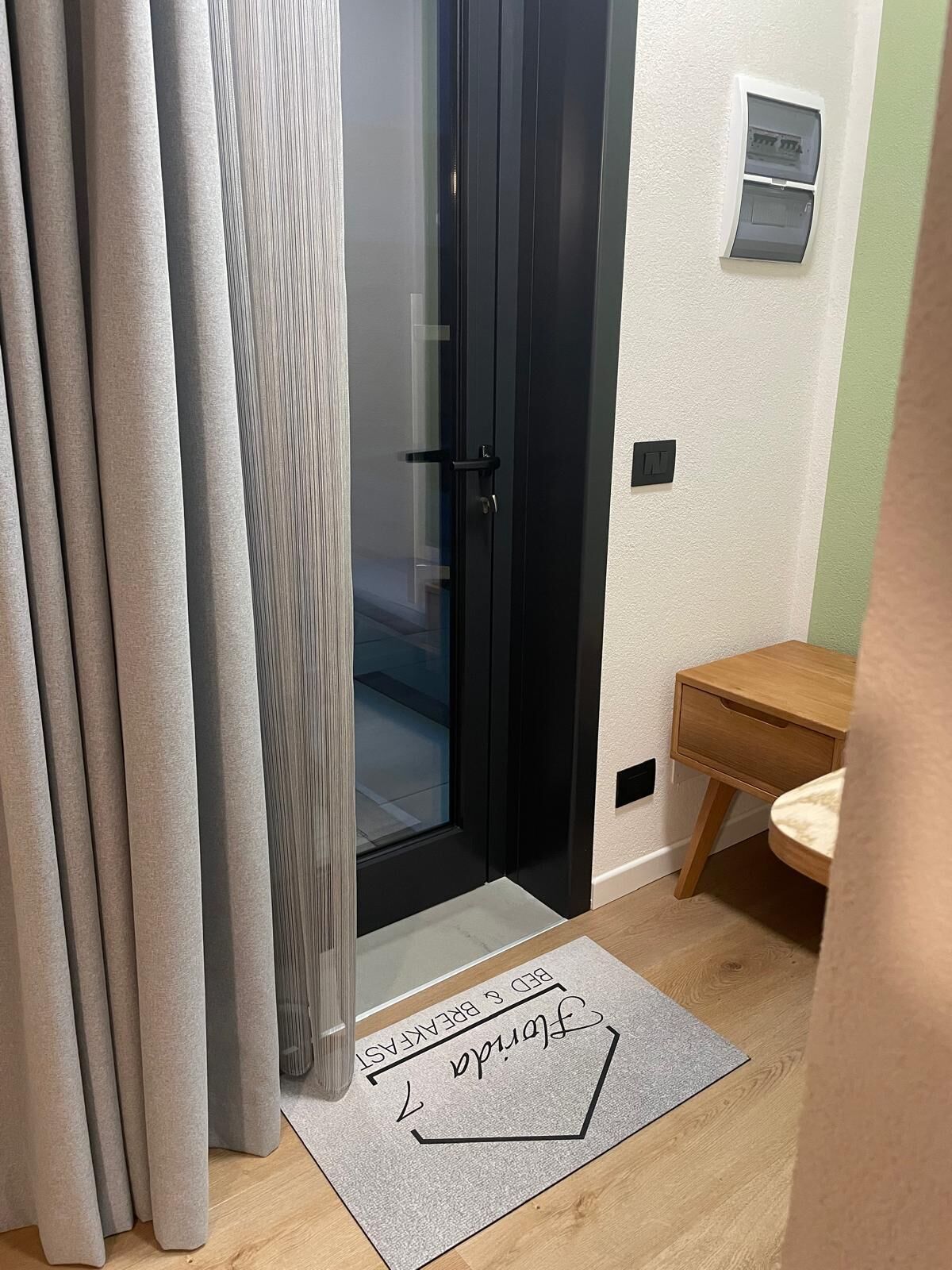 A room with a sliding glass door, a small wooden side table, and a doormat with text.
