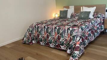 Un dormitorio con colcha estampada de flores, un gato en el suelo y cuadros en la pared.