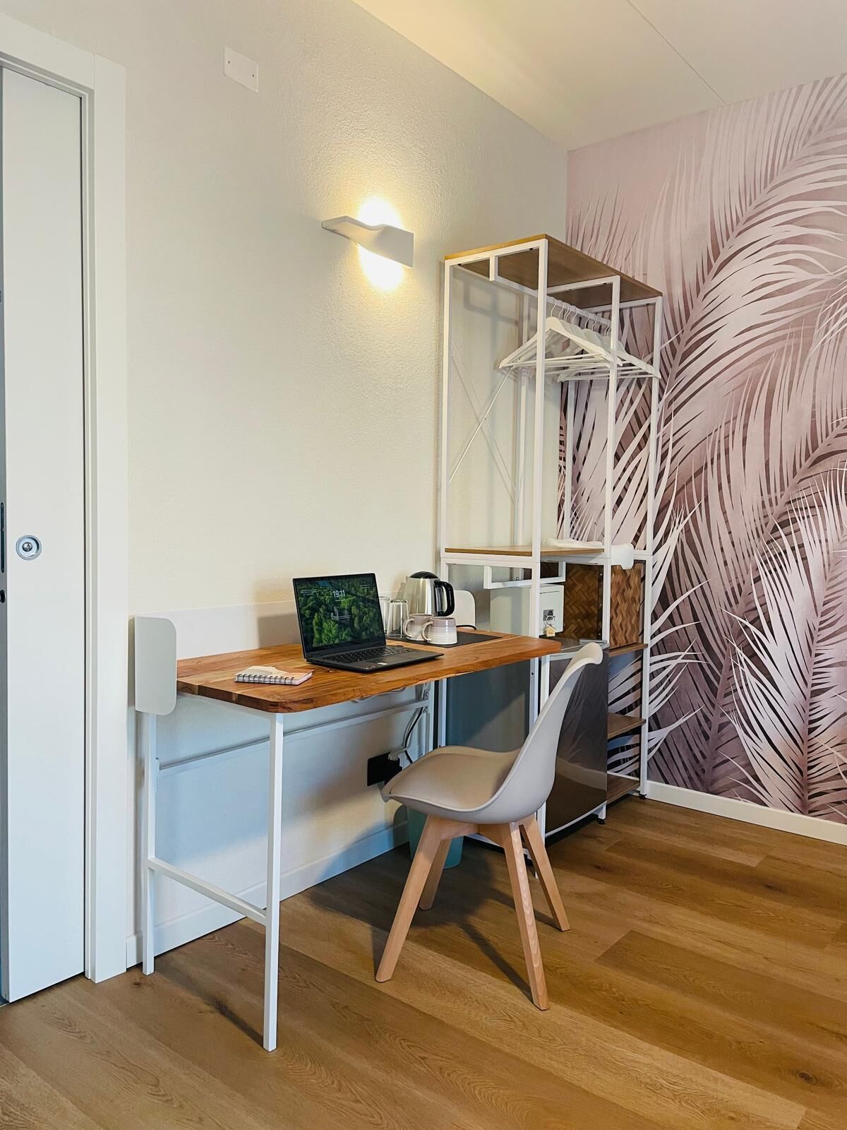 Une pièce de taille modeste, avec un bureau en bois, un ordinateur portable, une chaise blanche et une étagère fixée au mur.