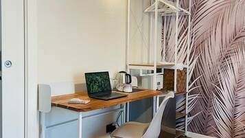Une pièce de taille modeste, avec un bureau en bois, un ordinateur portable, une chaise blanche et une étagère fixée au mur.