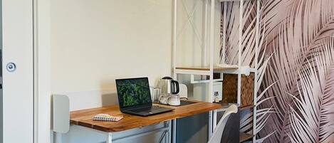 A compact room with a wooden desk, a laptop, a white chair, and a wall-mounted shelf.