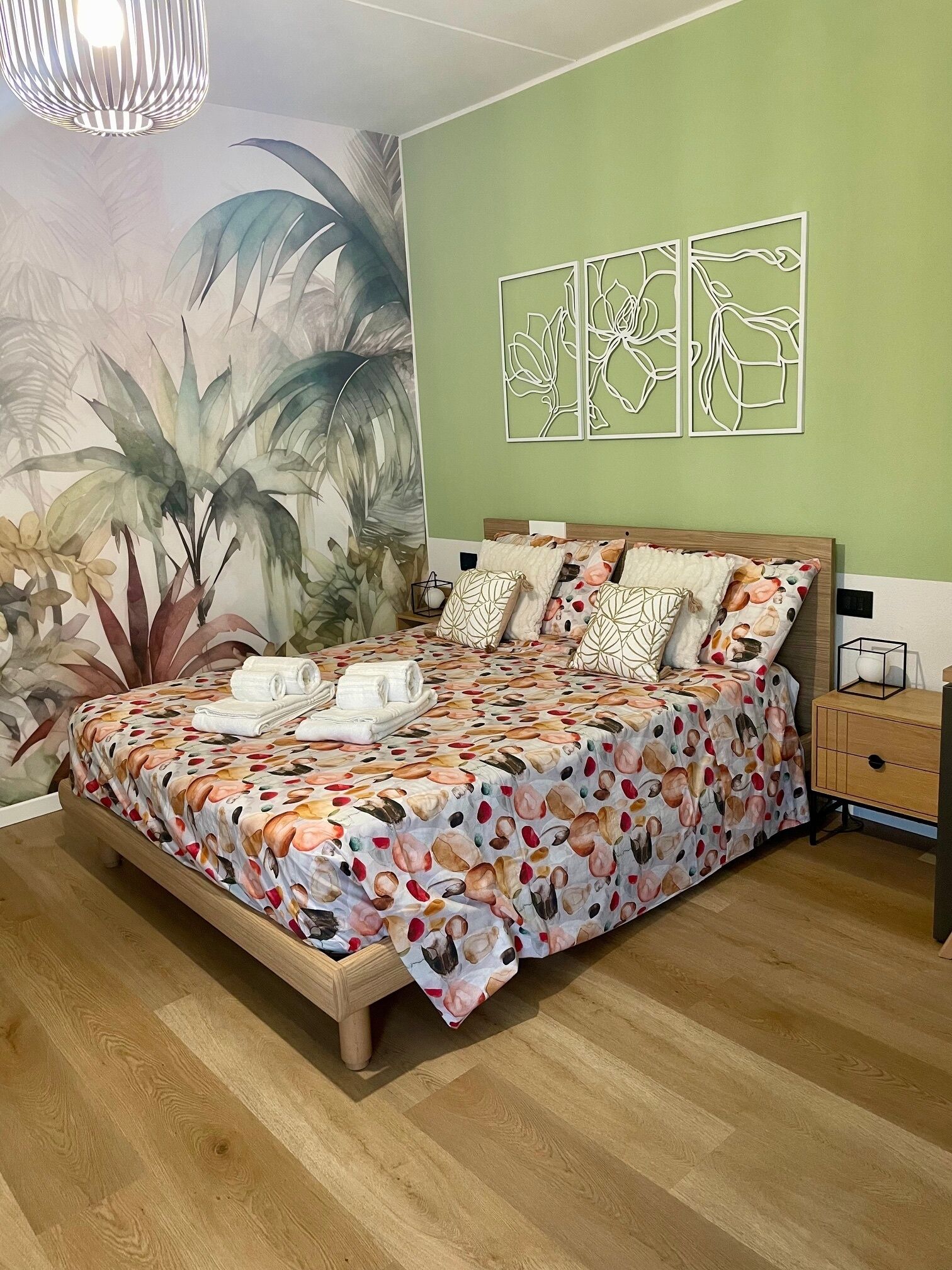 Un dormitorio con cama, mesita de noche, lámpara y un mural floral en la pared.