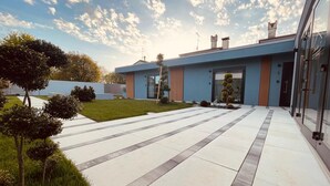 Un bâtiment moderne à la façade bleue, doté d’une entrée en verre et d’une cour dallée avec une pelouse.