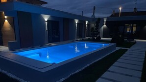 Une piscine extérieure moderne, dotée d’un design géométrique, entourée d’une pelouse bien entretenue et d’un chemin pavé.