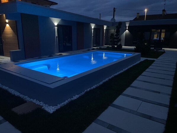A modern outdoor swimming pool with a geometric design, surrounded by a well-maintained lawn and a paved walkway. - FLORIDA 7 (Pertegada)