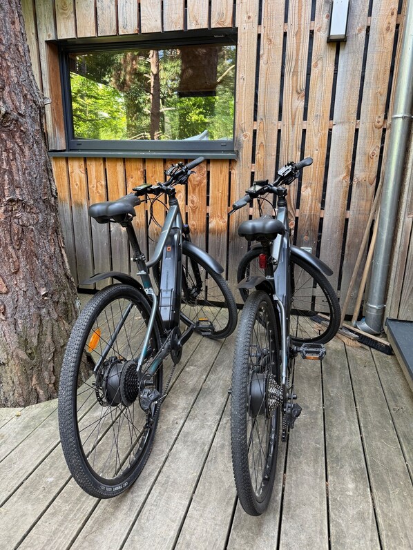 Twee mountainbikes staan geparkeerd op een houten terras voor een houten gebouw met een raam.