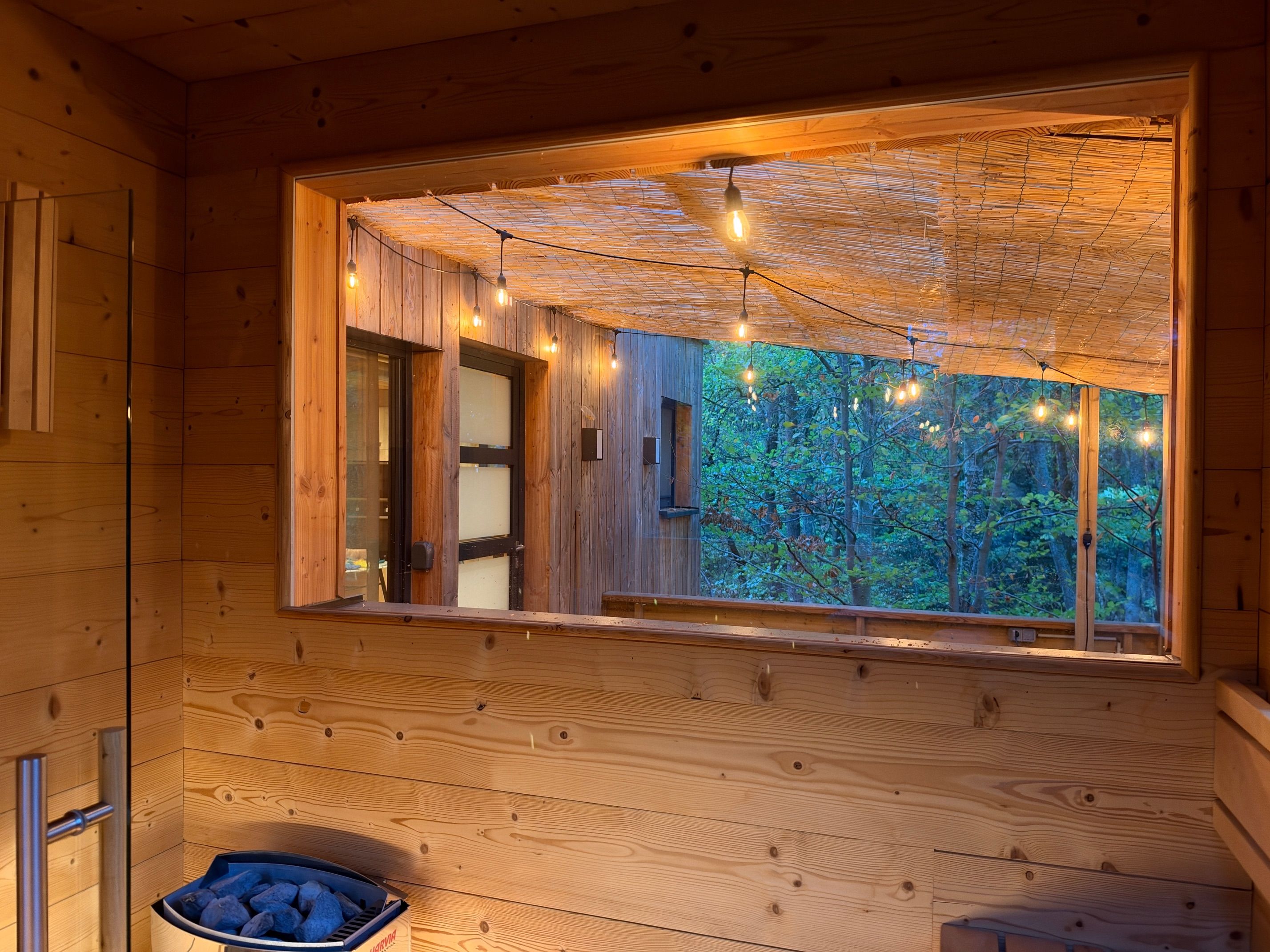 A wooden cabin interior with a large window, string lights, and a bucket of charcoal.