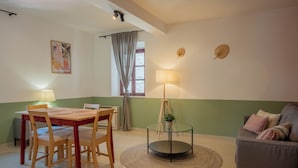 A dining area with a wooden table and chairs, a glass table lamp, a round rug, and a green wall. - Old Town Church Bells (Kotor)